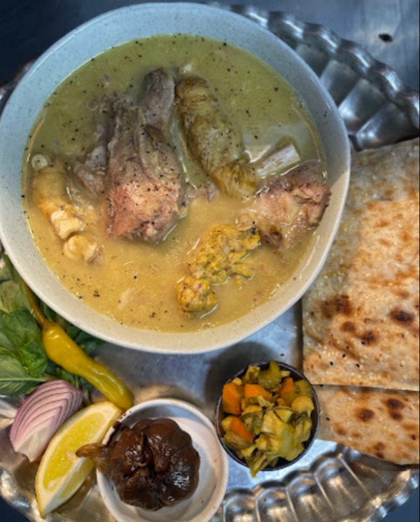 : Soofi Restaurant Kalle Pache with bread, lemon, herbs, onion, pickle, and dried fig.